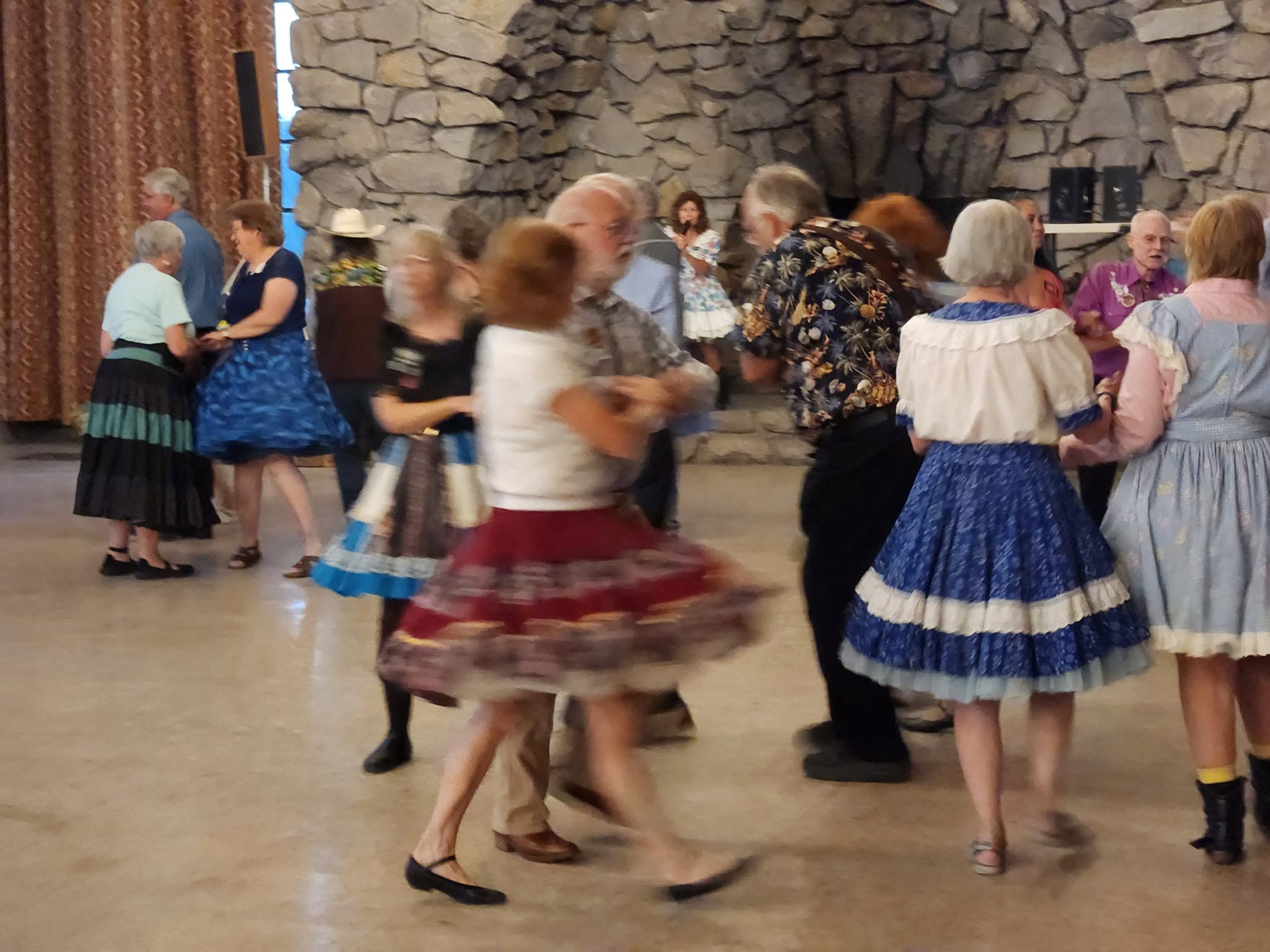 Square dancers turning with partners in front of the lodge fireplace